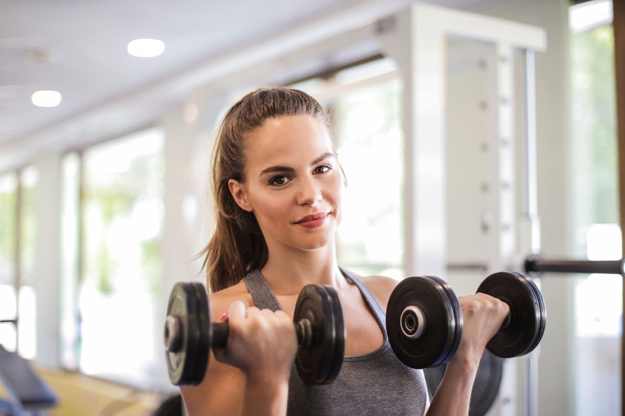 Woman exercising with dumbbells in a bright, modern gym, showcasing fitness and strength.