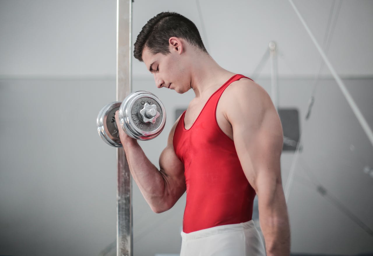 Muscular man in red outfit performing a dumbbell curl for strength training indoors.