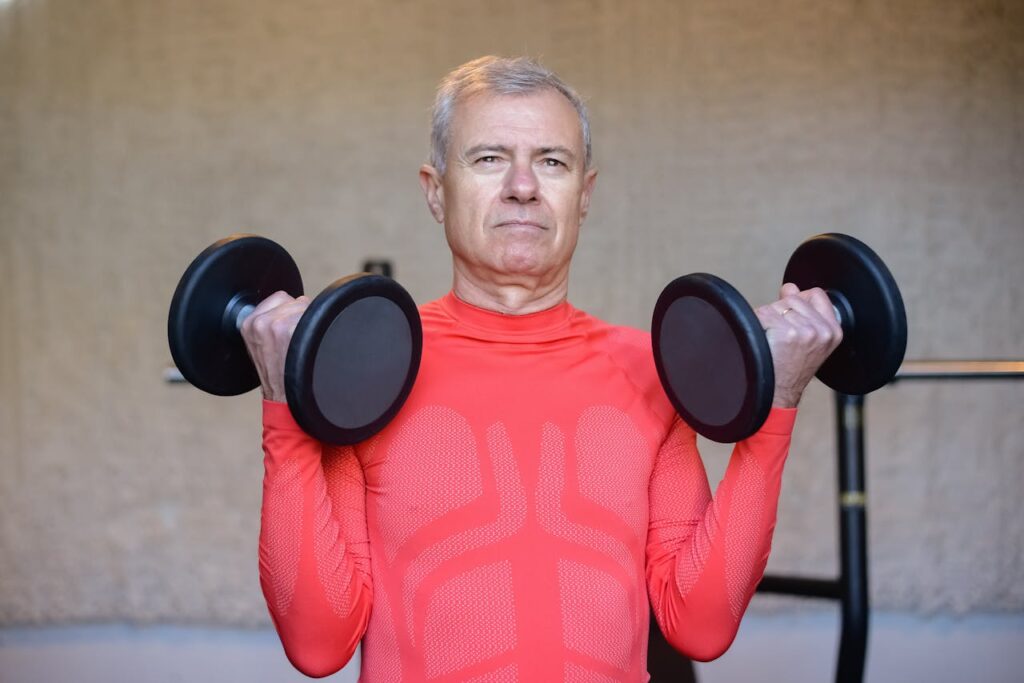 pexels photo 6922185 Elderly man in red lifting dumbbells, promoting fitness and healthy aging indoors.