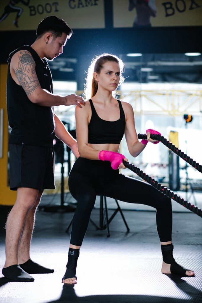 Dynamic scene of a woman training with battle ropes under instructor's guidance, focusing on strength and endurance.